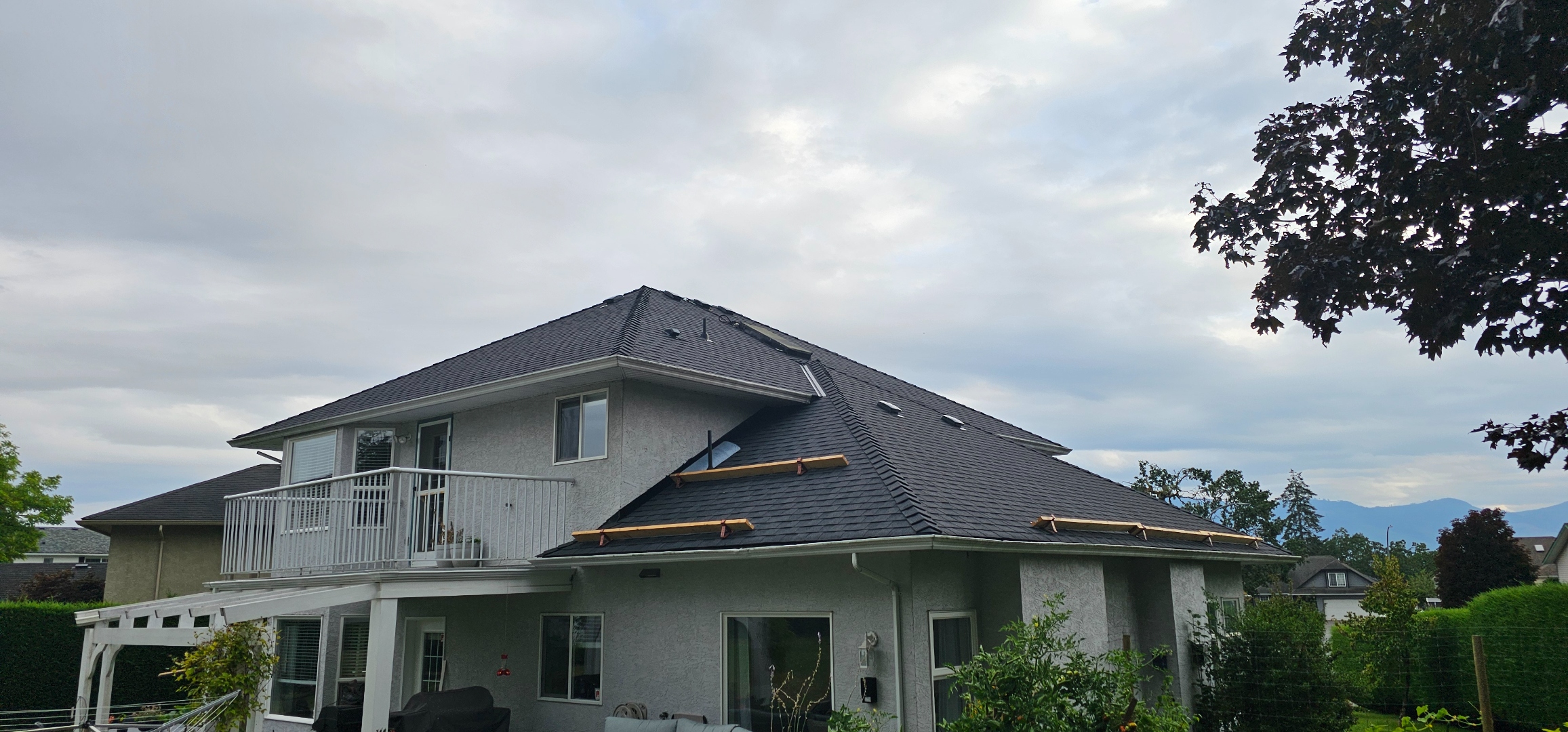 Large residential reroof — hip roof rear elevation, mountain backdrop